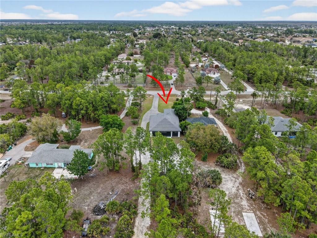 Aerial perspective showcasing a property surrounded by mature trees, featuring a paved driveway and a gray shingle roof