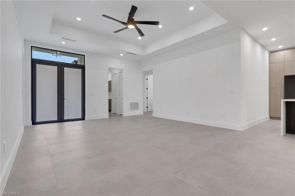Expansive interior space featuring a double-door entryway with frosted glass, tray ceiling, recessed lighting, ceiling fan, and large format tile flooring
