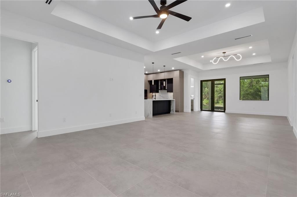 Spacious interior featuring large format tile flooring, tray ceilings with recessed lighting, and a contemporary ceiling fan