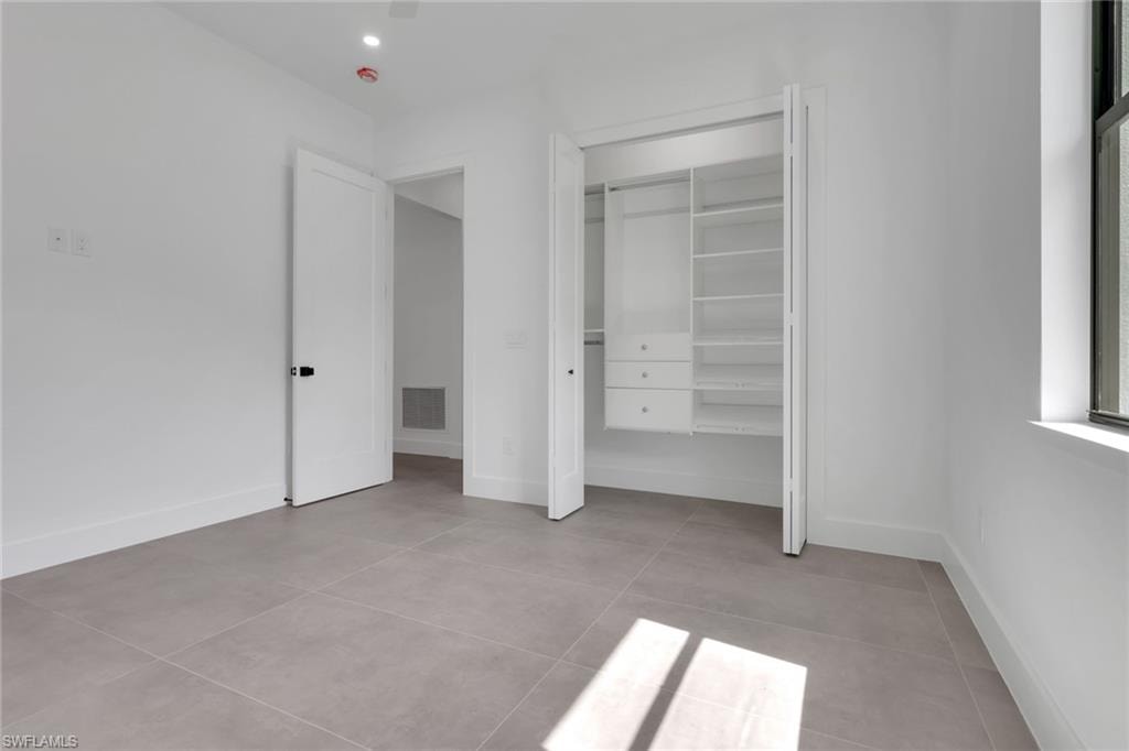 Spacious room featuring light gray tile flooring, crisp white walls, a built-in closet organization system with shelving and drawers, a large window, and a modern interior door with black hardware