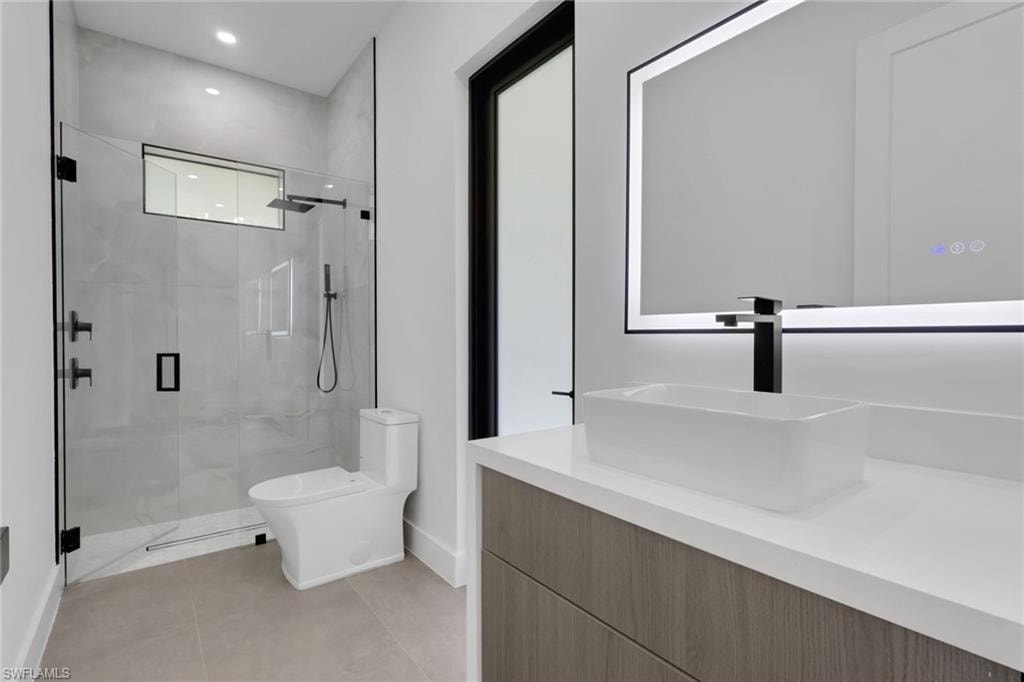Modern bathroom featuring a glass-enclosed shower, rain shower head, matte black fixtures, a rectangular vessel sink, and an illuminated mirror