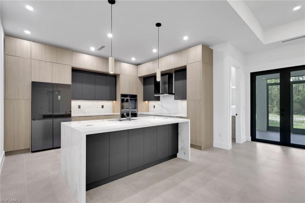 Modern kitchen featuring a waterfall island with a light stone countertop, flat-panel cabinetry in a two-tone finish, integrated refrigerator, and built-in wall oven