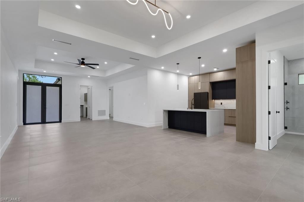 Open-concept living area with large format tile flooring and tray ceiling with recessed lighting