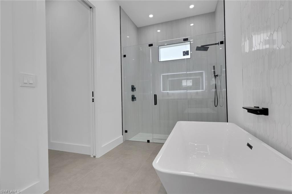 Modern bathroom featuring a freestanding tub, glass-enclosed shower with matte black fixtures, and light-toned geometric tile work