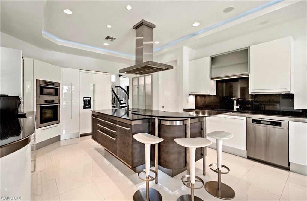 Kitchen with a kitchen breakfast bar, island range hood, decorative backsplash, stainless steel appliances, and a kitchen island