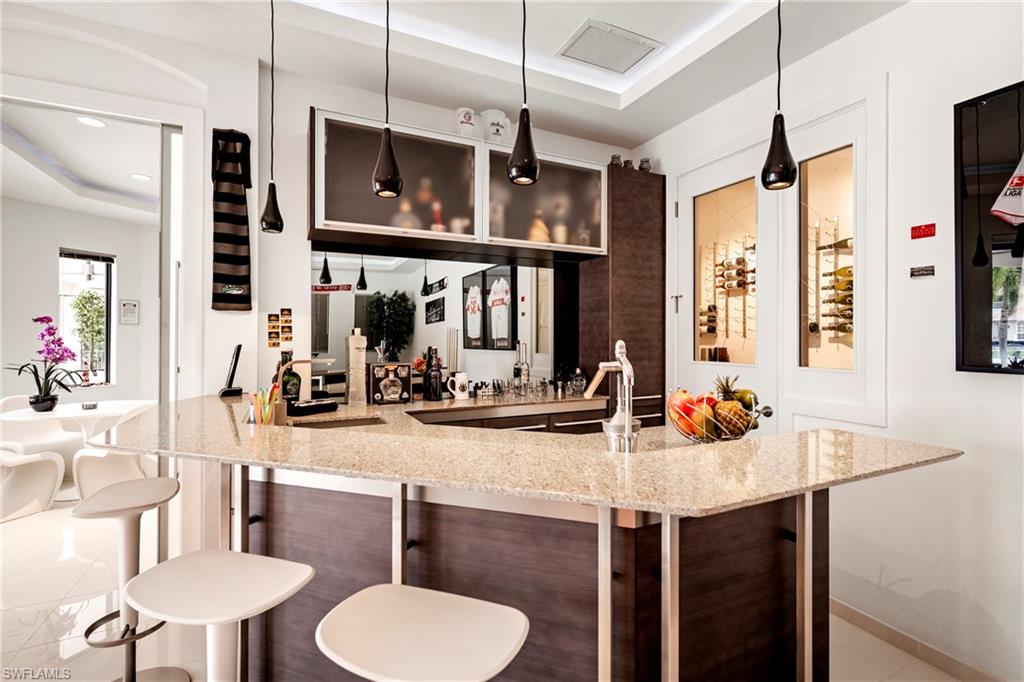Indoor wet bar featuring a tray ceiling, light stone countertops, decorative light fixtures, glass insert cabinets, and dark wood finish cabinetry