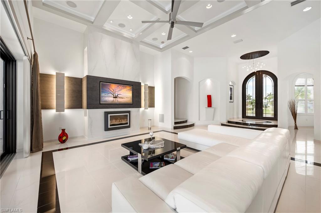 Living area featuring a premium fireplace, coffered ceiling, ceiling fan, arched walkways, and inlaid floor details