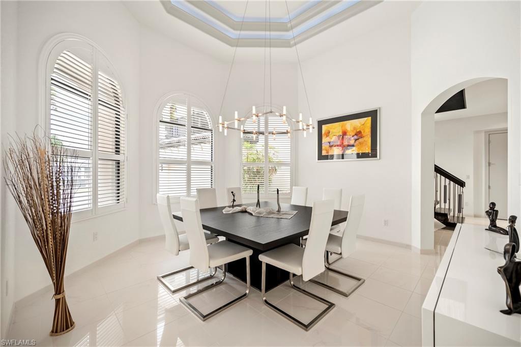 Dining area with arched walkways, a chandelier, a raised ceiling, and light tile patterned floors