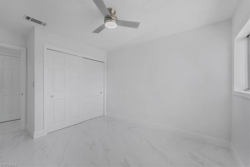 Unfurnished bedroom featuring light marble finish floors, a closet, and a ceiling fan