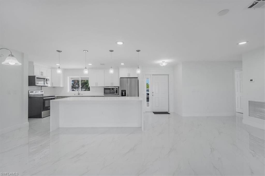 Kitchen featuring white cabinets, stainless steel appliances, a kitchen island, light stone countertops, and pendant lighting