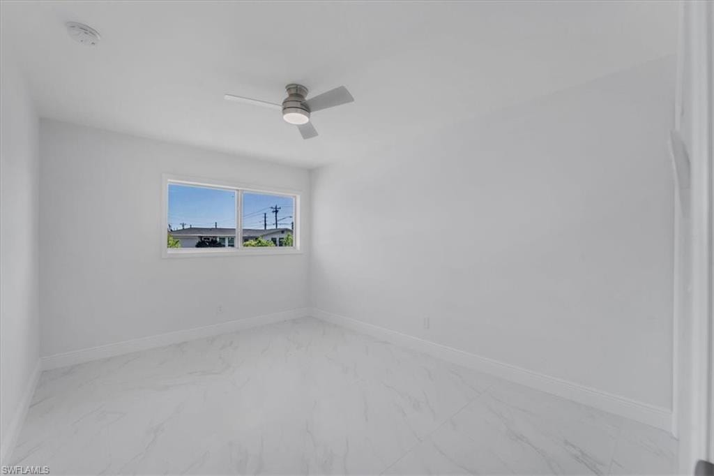 Unfurnished room featuring light marble finish floors, a ceiling fan, and a smoke detector