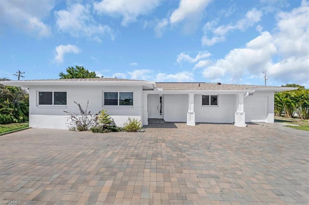 White stucco exterior featuring a covered entry porch with white columns, a paved driveway, and multiple windows