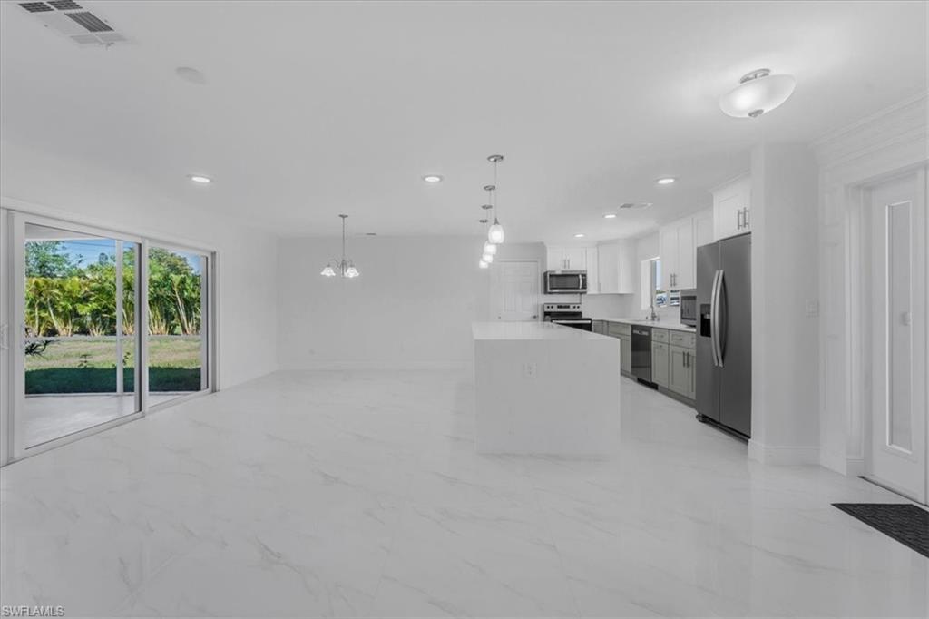 Kitchen featuring stainless steel appliances, light marble finish floors, a chandelier, open floor plan, and white cabinetry