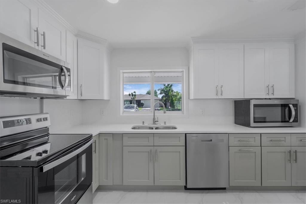 Kitchen featuring stainless steel appliances, dual tone cabinetry, and light stone counters
