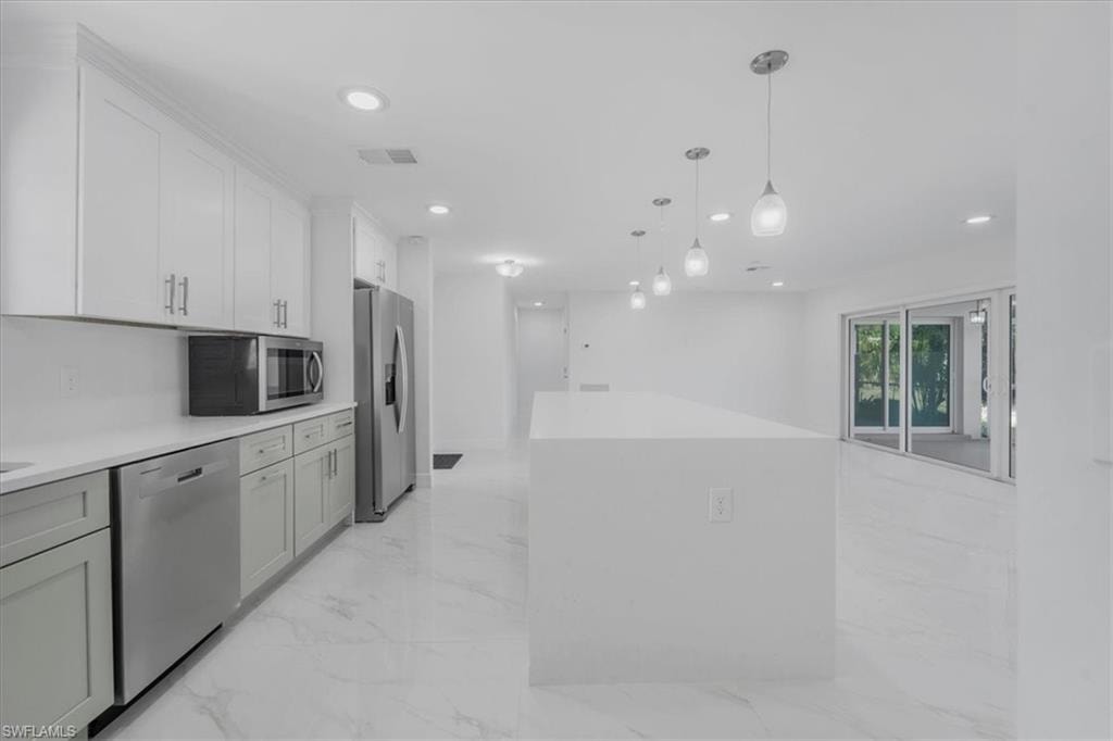 Kitchen with stainless steel appliances, pendant lighting, white cabinets, and light stone counters