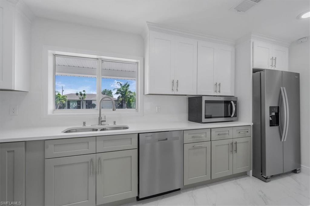 Kitchen featuring stainless steel appliances, light marble finish flooring, white cabinetry, and gray cabinets