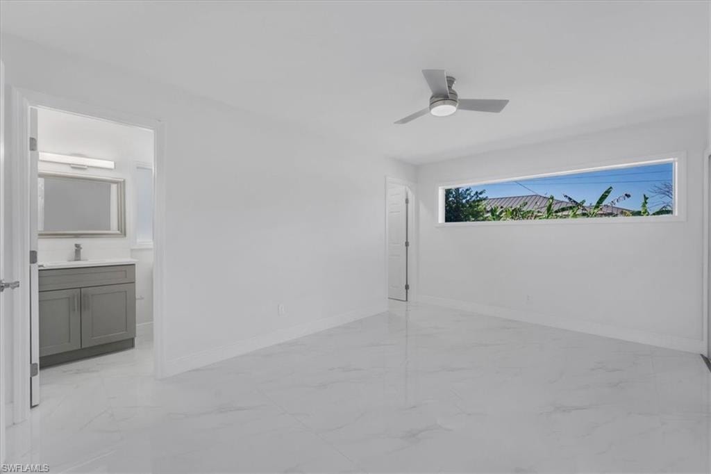 Unfurnished bedroom featuring light marble finish flooring, ceiling fan, and ensuite bathroom