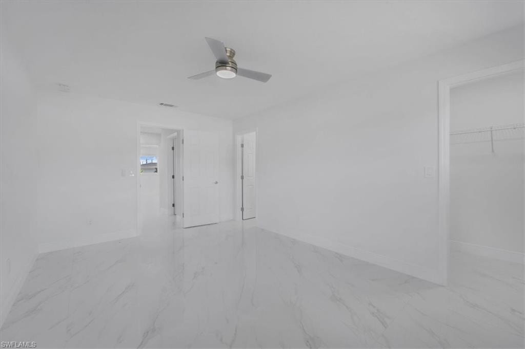 Unfurnished room with ceiling fan and light marble finish floors
