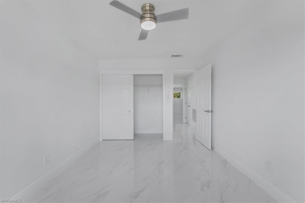 Unfurnished bedroom with a closet, light marble finish floors, and ceiling fan