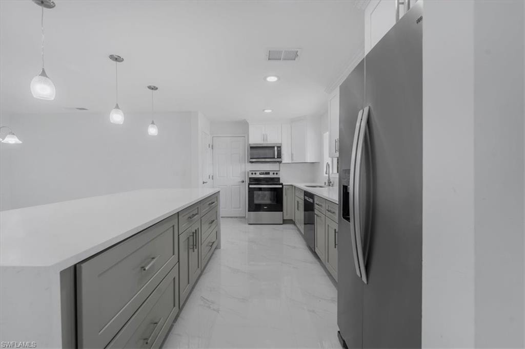 Kitchen with stainless steel appliances, two tone cabinetry, light stone countertops, hanging light fixtures, and a kitchen island
