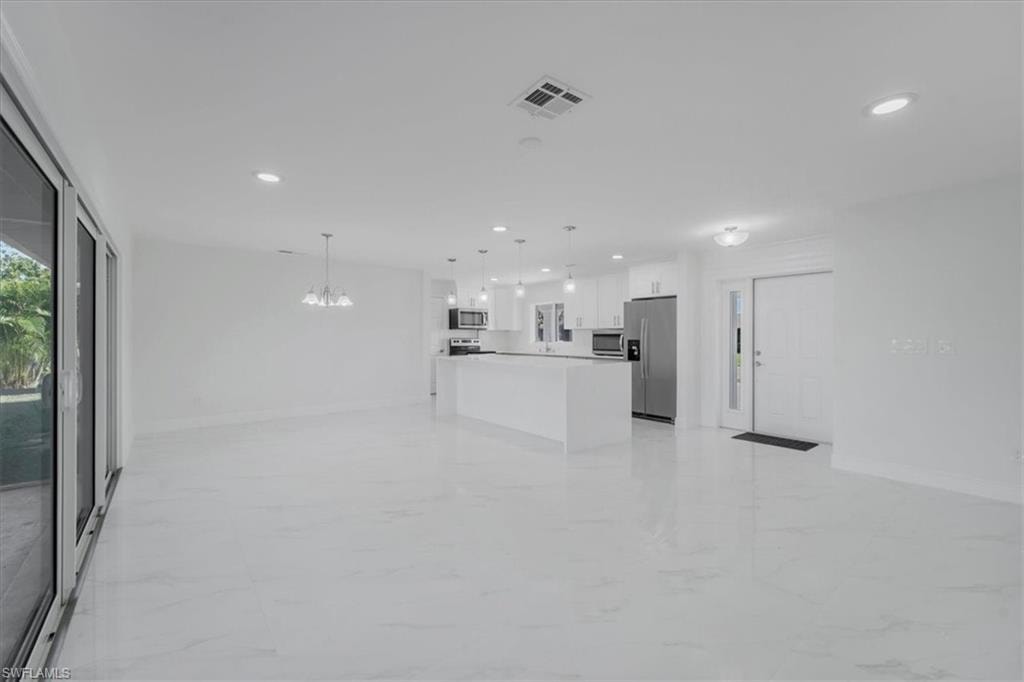 Unfurnished living room featuring light marble finish floors and hanging lights
