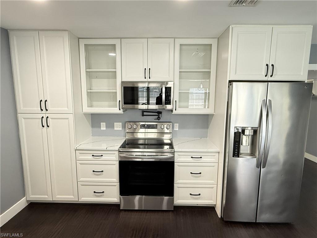 Kitchen featuring stainless steel appliances, white cabinets, light stone countertops, and dark wood-style floors