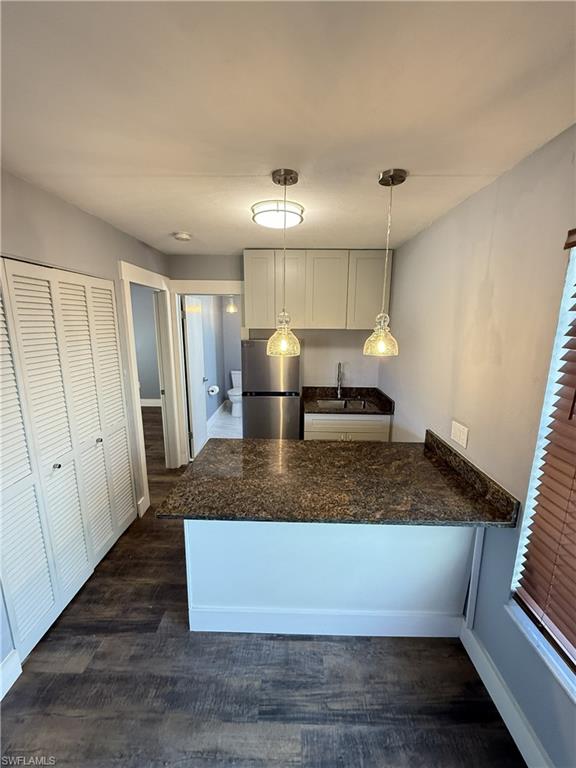 Guest House, Kitchen with a peninsula, dark wood-type flooring, freestanding refrigerator, white cabinets, and a breakfast bar area