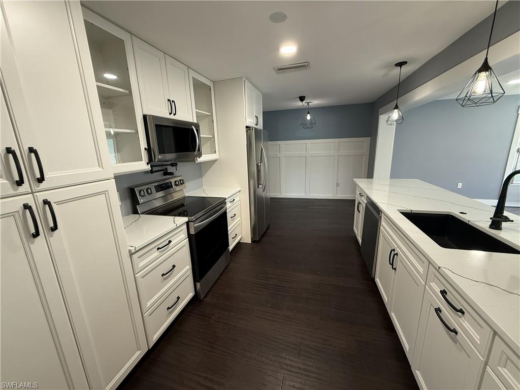 Kitchen featuring stainless steel appliances, white cabinets, light stone countertops, glass fronted cabinets, and dark wood-type flooring