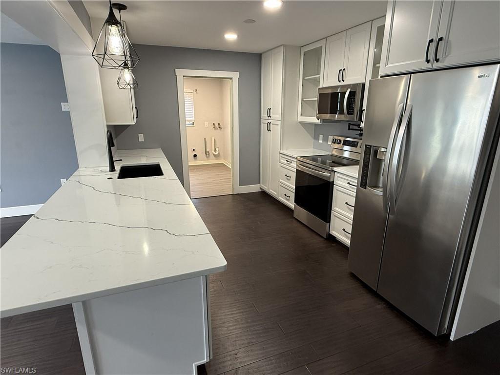 Kitchen with stainless steel appliances, light stone counters, dark wood finished floors, white cabinets, and glass fronted cabinets
