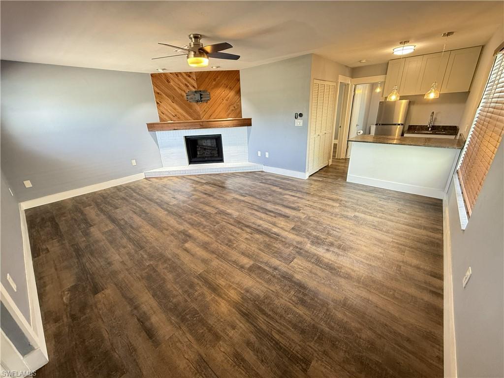 Guest House, Unfurnished living room with dark wood-type flooring, ceiling fan, and a fireplace with raised hearth