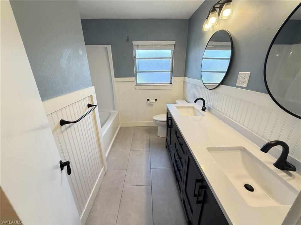 Bathroom featuring wainscoting, double vanity, and light tile patterned flooring