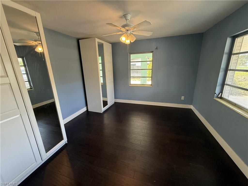 Unfurnished bedroom featuring multiple windows, dark wood finished floors, a ceiling fan, and a closet
