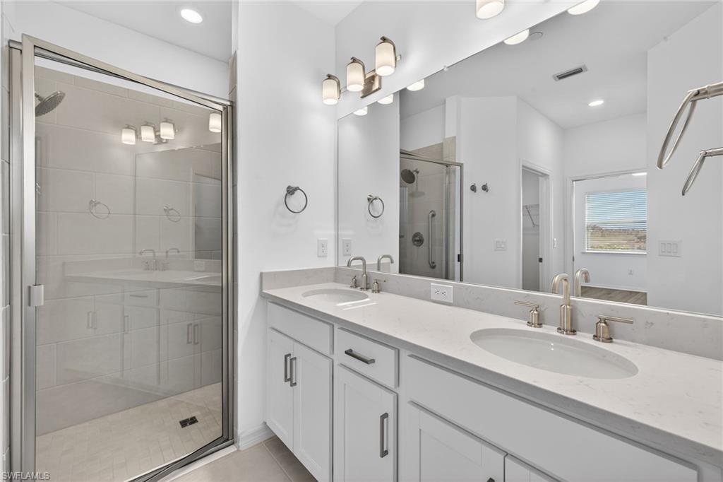 Full bath featuring double vanity, a shower stall, recessed lighting, light tile patterned floors, and a spacious closet