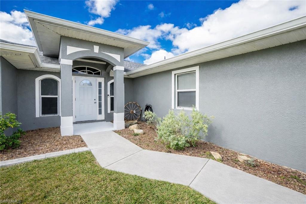 View of exterior entry with stucco siding and a yard