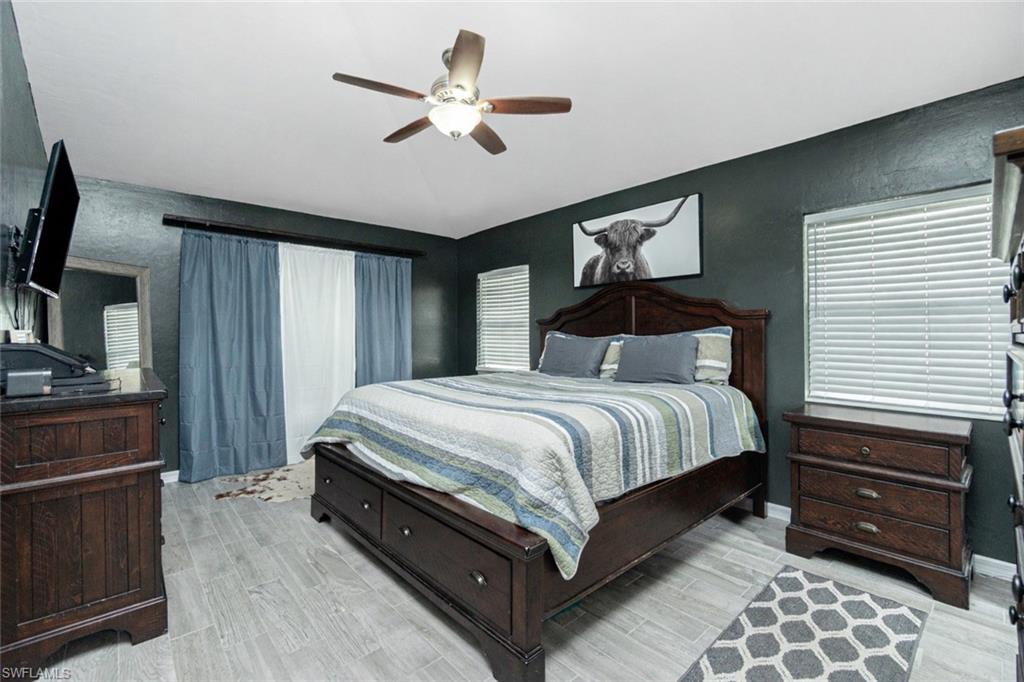 Bedroom featuring light wood finished floors, a ceiling fan, a textured wall, and vaulted ceiling