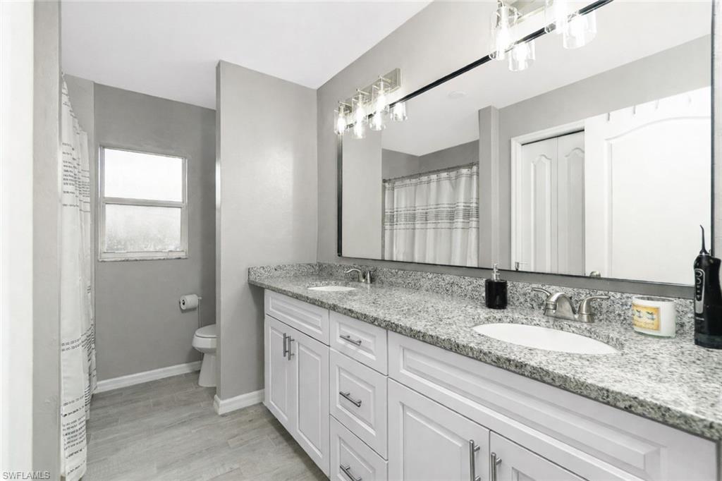 Full bath with double vanity, curtained shower, light wood-style flooring, and a closet