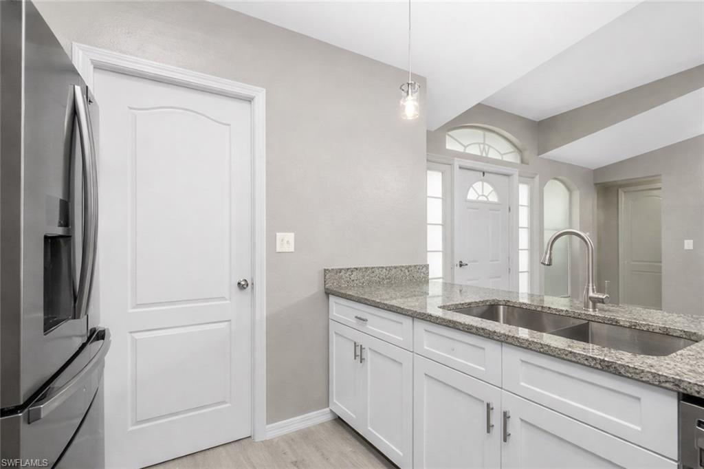 Kitchen with stainless steel fridge, light stone counters, white cabinetry, pendant lighting, and light wood-type flooring