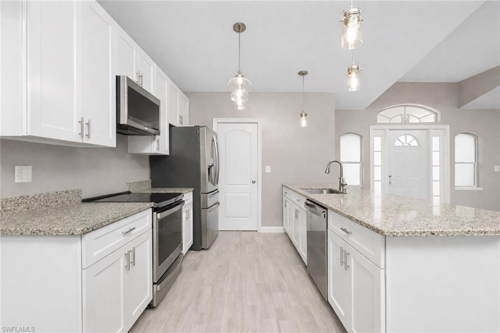 Kitchen with stainless steel appliances, white cabinetry, light stone countertops, light wood-style flooring, and hanging light fixtures