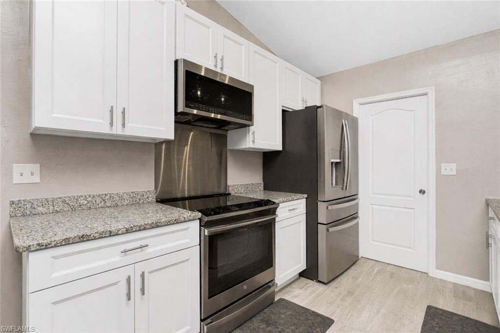 Kitchen with stainless steel appliances, white cabinets, and light stone countertops