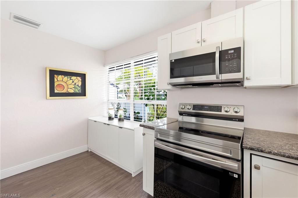 Kitchen with stainless steel appliances, white cabinetry, dark wood-style flooring, and dark countertops