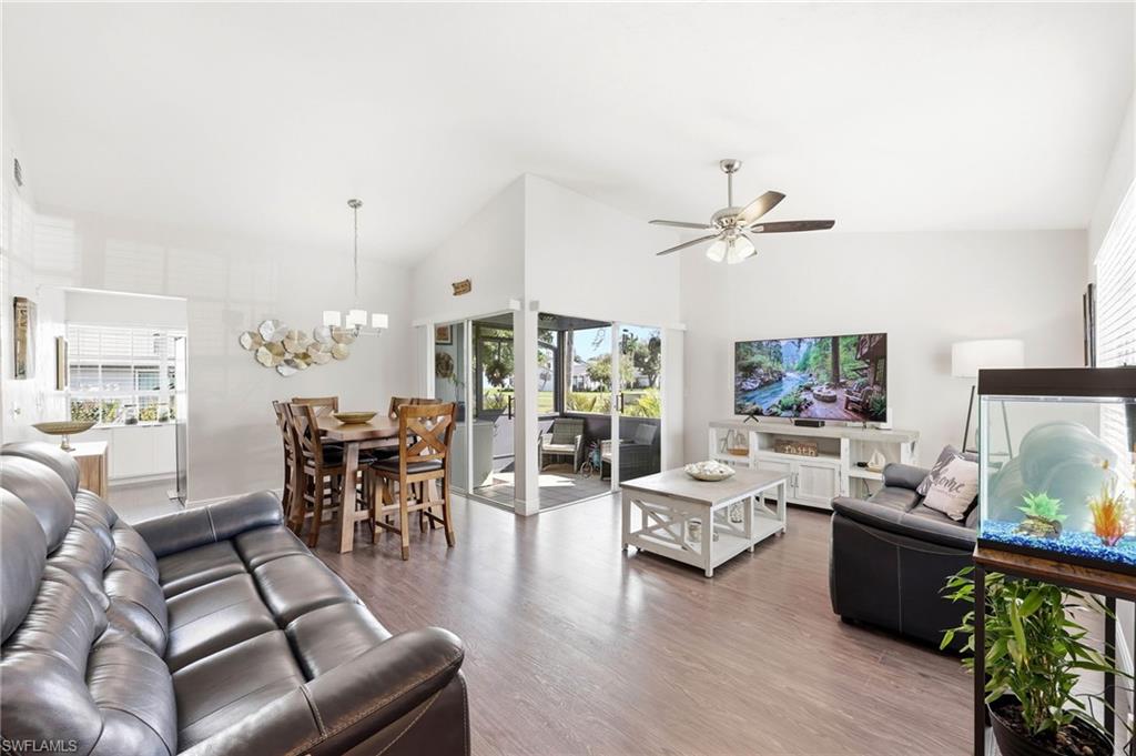 Living room with wood finished floors, vaulted ceiling, plenty of natural light, a ceiling fan, and hanging lights