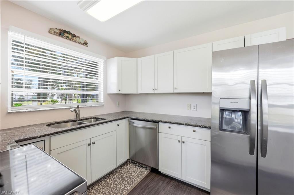 Kitchen with stainless steel appliances, white cabinets, dark stone countertops, and dark wood-style floors