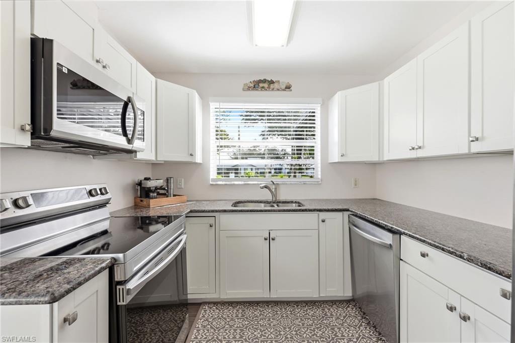 Kitchen with stainless steel appliances, white cabinets, and dark stone countertops
