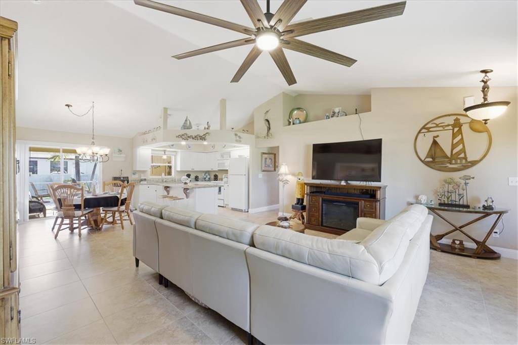 Living room featuring lofted ceiling, suspended lighting, a glass covered fireplace, light tile patterned floors, and a ceiling fan
