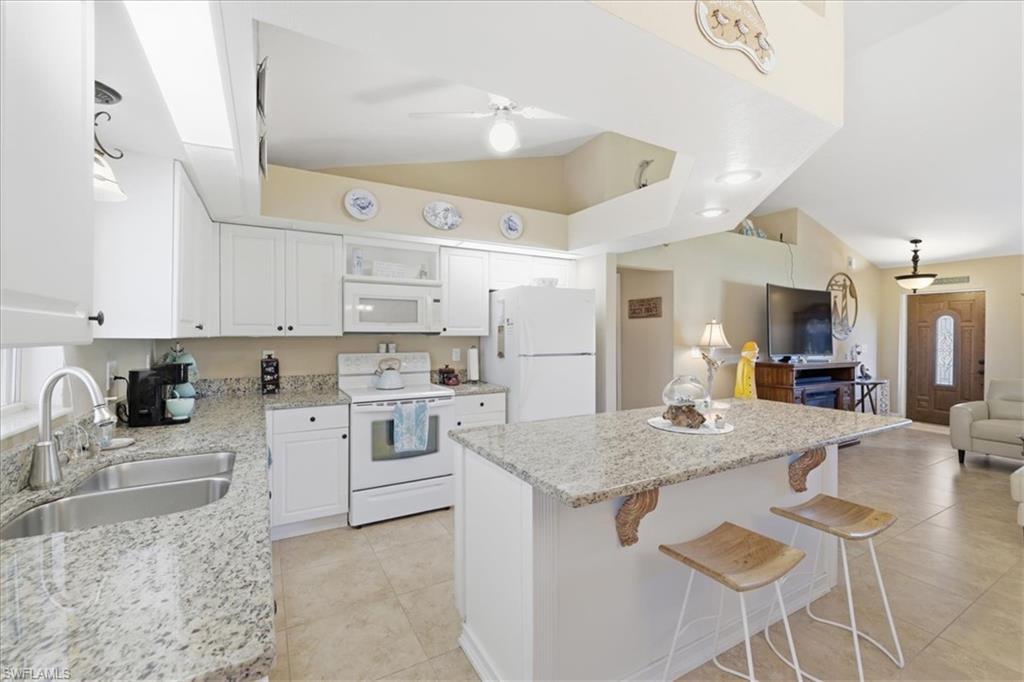 Kitchen with open floor plan, a kitchen breakfast bar, white appliances, white cabinets, and lofted ceiling