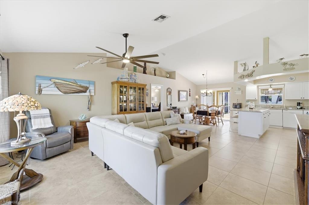 Living room featuring ceiling fan, light tile patterned floors, a chandelier, and lofted ceiling