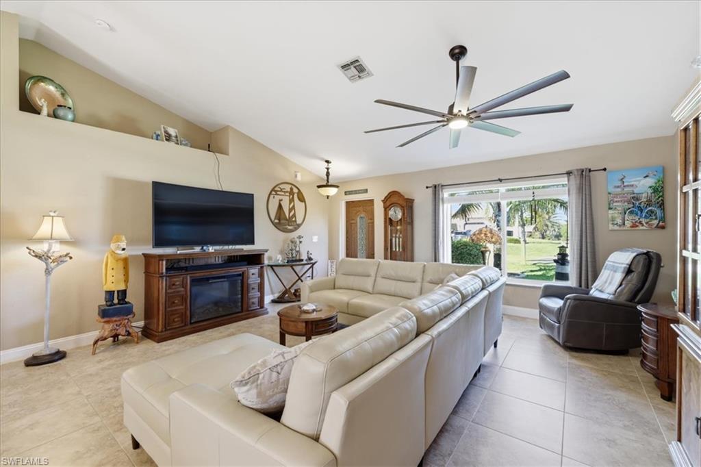 Living area featuring lofted ceiling, a ceiling fan, light tile patterned flooring, and a glass covered fireplace