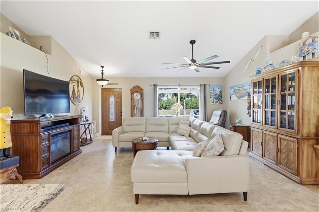 Living room with lofted ceiling, a ceiling fan, a glass covered fireplace, and light tile patterned floors