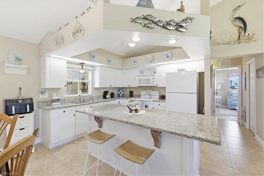 Kitchen featuring a breakfast bar, white cabinetry, light stone counters, white appliances, and a kitchen island