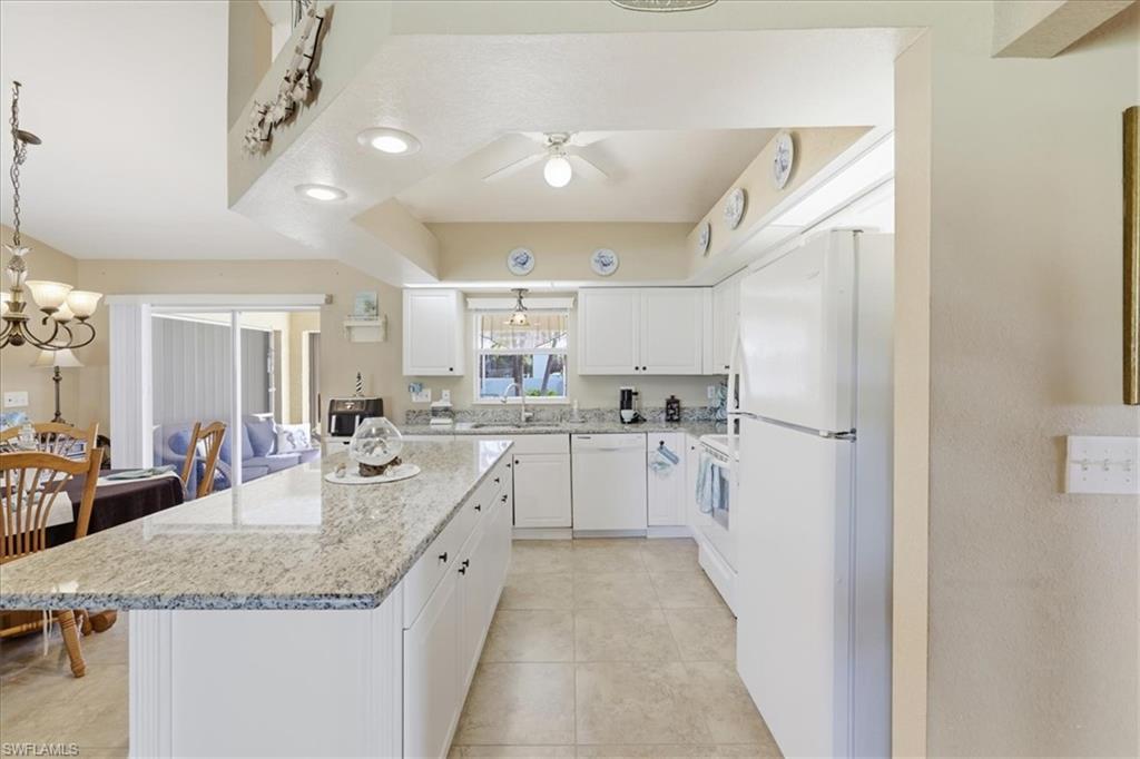 Kitchen featuring white cabinetry, white appliances, hanging lights, light stone counters, and a center island
